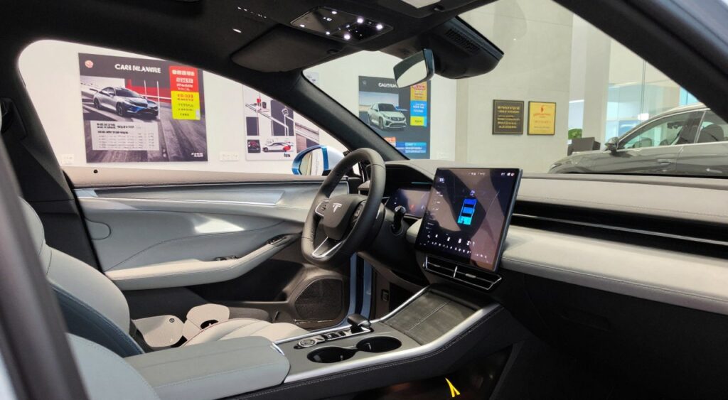 A detailed view of modern vehicle safety features in an automotive showroom setting. In the foreground, open car doors reveal high-tech dashboards with advanced safety displays, airbags, and seatbelt systems visible. In the middle ground, a sleek car sits under bright, soft LED lighting, showcasing features like adaptive cruise control, lane departure warning sensors, and a rear-view camera. The background includes posters of crash test ratings and safety accolades, conveying a sense of reliability and innovation. The composition is shot from a slightly elevated angle, highlighting the interior and exterior simultaneously, with reflections adding a glossy finish. The overall mood is professional and informative, emphasizing the importance of safety in modern vehicles.